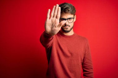 Kırmızı arka planda duran sakallı ve süveterli yakışıklı genç adam avucunun içinde şarkı söylemeyi kesiyor. Yüzünde olumsuz ve ciddi bir jest olan uyarı ifadesi.