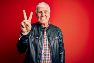 Kıdemli yakışıklı, beyaz gömlekli ve ceketli adam izole edilmiş kırmızı arka planda iki numarayı gösterirken kendinden emin ve mutlu bir şekilde gülümsüyor..