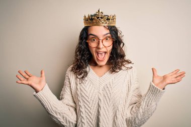 Kıvırcık saçlı, beyaz arka planda altın kraliçenin tacını takan genç ve güzel bir kadın çılgın ve başarıyı kollarını kaldırıp heyecanla haykırarak kutluyor. Kazanan konsept
