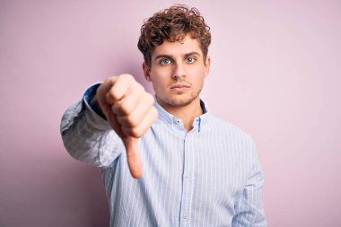 Sarışın, kıvırcık saçlı, beyaz arka planda çizgili tişört giyen mutsuz ve sinirli görünen, reddedilmiş ve olumsuz jestli genç bir adam. Kötü ifade.