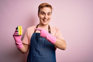 Önlük ve eldiven giyerek ev işi yapan yakışıklı kızıl adam daha temiz bir fırça kullanıyor.