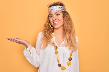 Mavi gözlü, güneş gözlüklü, aksesuarlı, neşeli gülümseyen, eli kameraya bakan güzel sarışın hippi kadın..