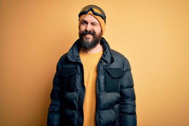 Sakallı, kar maskeli, kar maskeli ve kar gözlüklü yakışıklı kayakçı. Kameraya seksi bir ifadeyle bakıyor. Neşeli ve mutlu bir yüzü var..