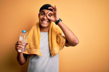 Genç ve yakışıklı Afro-Amerikan sporcusu havluyla gülen yüzlü bir şişe su içiyor.