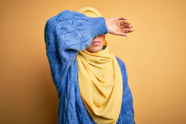 年轻美丽的黑发穆斯林女子 头戴阿拉伯头巾 用胳膊遮住孤立的黄色背景 眼神严肃而忧郁 目光短浅 躲藏和拒绝的概念 — 图库照片