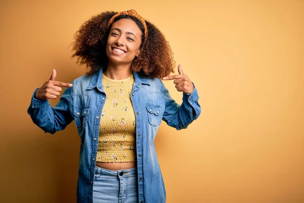 Beautiful african american with afro hair standing over yellow isolated background looking confident with smile on face, pointing oneself with fingers proud and happy.