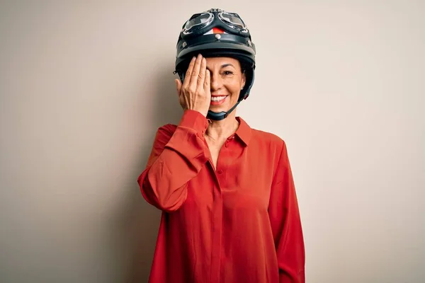 中年オートバイの女性身に着けていますオートバイヘルメット上の隔離された白い背景カバー1目で手 顔に自信を持って笑顔と驚きの感情 — ストック写真