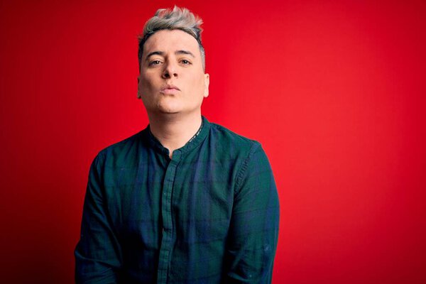 Young handsome modern man wearing elegant green shirt over red isolated background looking at the camera blowing a kiss on air being lovely and sexy. Love expression.