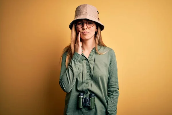 歯痛や歯の病気のために痛みを伴う表現で手に触れる双眼鏡を使用して帽子や眼鏡を着用青い目を持つ美しいブロンドの探検家の女性 歯医者 — ストック写真
