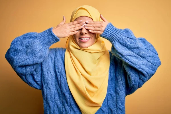 若い美しいブルネットのイスラム教徒の女性は 明るく面白い笑みを浮かべて手で目をカバー孤立した黄色の背景の上にアラブヒジャーブを身に着けています ブラインドコンセプト — ストック写真