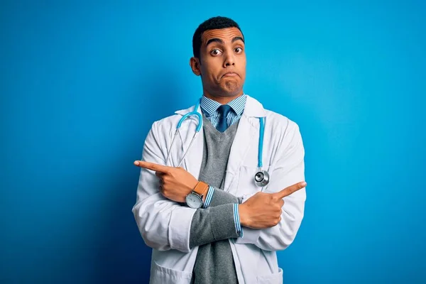英俊的非洲裔美国医生 身穿外套和听诊器 头戴蓝色背景的男子 手指指向两边 方向不一 — 图库照片