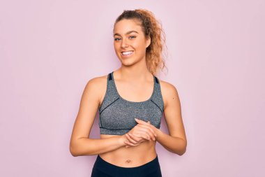 Mavi gözlü genç, güzel sarışın spor kadın spor kıyafetleri giyiyor ve ellerini kavuşturup gülümsüyor. Başarı ve iyimser