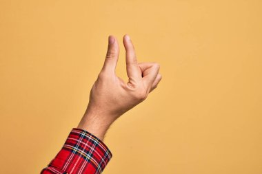 İzole edilmiş sarı arka plan üzerinde parmaklarını gösteren beyaz bir adamın eli. Görünmez bir şeyi alıp, parmaklarıyla uzayı gösteren bir nesneyi tutuyor.
