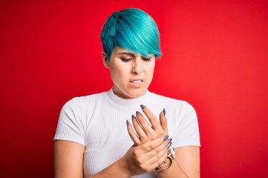 Mavi saçlı, kırmızı arka planda sıradan tişörtler giyen genç ve güzel bir kadın. Ellerinde ve parmaklarında ağrı, iltihaplanma.