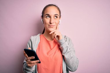 Spor yapan güzel bir kadın müzik dinliyor. Kulaklıkları pembe arka planda kullanıyor. Ciddi bir yüz.