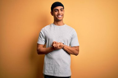 Yakışıklı Afro-Amerikan sporcu sarı arka planda spor giysisi giyiyor ve parmaklarını çapraz yapıp gevşek ve neşeli gülümsüyor. Başarı ve iyimser