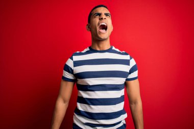 Yakışıklı Afro-Amerikan erkeği, sıradan çizgili tişörtler giymiş, kırmızı arka planda öfkeli ve sinirli bir şekilde bağırıyor, öfkeyle bağırıyor. Öfke ve agresif kavram.