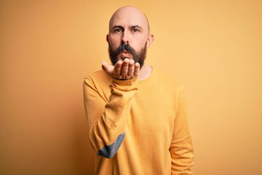 Sarışın, sakallı, sıradan bir kazak giyen yakışıklı bir adam sarı arka planda dikilip kameraya bakarken havada el sallayan bir öpücük veriyor. Güzel ve seksi. Aşk ifadesi.