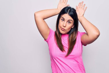 Genç, güzel, esmer, günlük pembe tişörtler giyen, beyaz arka planda duran, avuçlarında alaycı ve kuşkucu ellerle tavşan kulağı hareketi yapan bir kadın. Paskalya tavşanı kavramı.