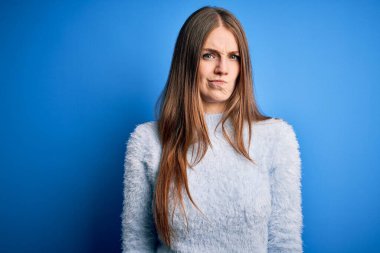 Genç, güzel, kızıl saçlı bir kadın, izole edilmiş mavi arka plan kuşkucu ve gergin üzerine sıradan bir süveter giyiyor, sorun yüzünden surat asıyor. Negatif kişi.