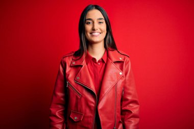 Genç, güzel, esmer, sıradan bir ceket giyen, mutlu ve havalı bir gülümsemeyle izole edilmiş kırmızı arka planda duran bir kadın. Şanslı kişi..