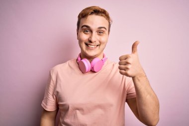 Genç, kızıl saçlı, müzik dinleyen pembe arka planda kulaklık takan mutlu bir el hareketi yapan yakışıklı bir adam. Kameraya bakıp başarıyı gösteren ifade onaylanıyor.