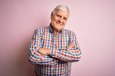 Soyutlanmış pembe arka planda, kollarını kavuşturup kameraya bakarken gülümseyen son sınıf yakışıklı, beyaz gömlekli adam. Pozitif kişi.