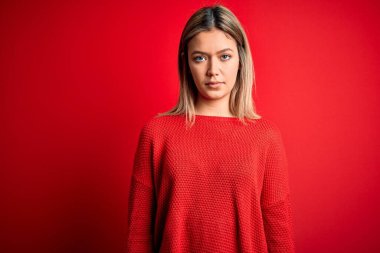 Kırmızı izole edilmiş arka plan üzerine sıradan bir süveter giyen genç, güzel sarışın kadın yüzünde ciddi bir ifadeyle rahatlamış. Basit ve doğal bir şekilde kameraya bakıyorsun..