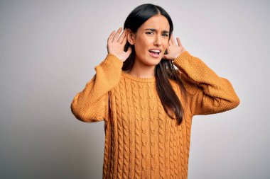 İzole edilmiş beyaz arka plan üzerine gündelik kazak giyen genç, güzel esmer kadın iki elini de kulak hareketi yaparken duymaya çalışıyor, dedikoduya meraklı. İşitme problemi, sağır