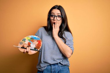 Genç esmer kadın ressam elinde boya fırçası ve palet ile sarı arka plan kapağının üzerinde resim yapıyor. Ağzı, hata yüzünden utançla kaplı, korkunun ifadesi, sessizlikten korkmak, gizli bir konsept.