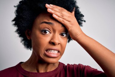 Beyaz arka planda duran kıvırcık saçlı, genç ve güzel Afro-Amerikan kadın, elleri başının üstünde, utanç ve şaşkınlık dolu, sinirli ve hayal kırıklığına uğramış. Hata için korku ve üzüntü.