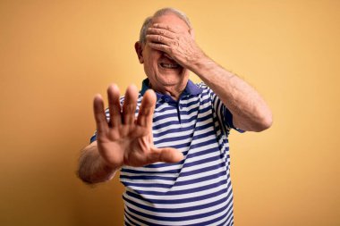 Gri saçlı, donanma tişörtü giyen, sarı arka planda duran, gözleri ellerle kaplayan, üzgün ve korku ifadesiyle dur hareketi yapan son sınıf öğrencisi. Utanç verici ve olumsuz bir kavram..