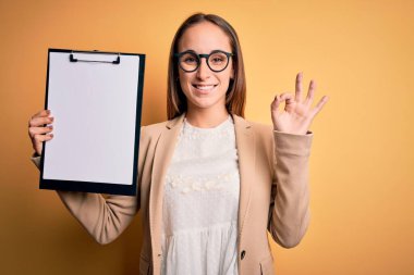Sarı arka planda gözlük takan güzel müfettiş kadın tamam işareti yapıyor, mükemmel bir sembol.