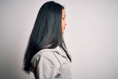 Genç, güzel, Çinli sporcu kadın, izole edilmiş beyaz arka planda eşofman üstü giyer, yan yana bakar, rahat poz verir, kendine güler yüzlü, doğal bir yüz takınır..