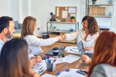 Bir grup iş adamı mutlu ve kendinden emin gülümsüyor. Birlikte çalışırken gülümseyerek ofiste el sıkışırken.