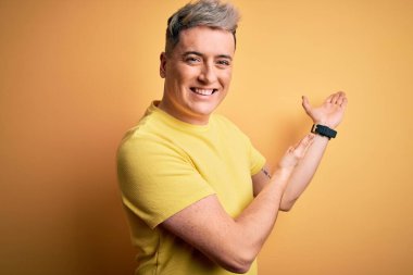 Sarı arka plan üzerine sarı tişört giyen yakışıklı modern bir adam gülümseyerek doğal bir şekilde içeri girmeye davet ediyor.