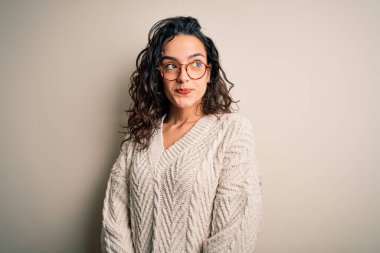 Kıvırcık saçlı, günlük süveter giyen, beyaz arka planda gözlük takan, gülümseyen ve kafasını çeviren güzel bir kadın..