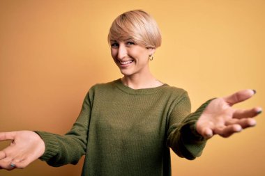 Sarışın, modern kısa saçlı, sarı arka planda rahat süveter giyen neşeli gülümsemeli, yardım eli uzatan ve kabul gören genç bir kadın..