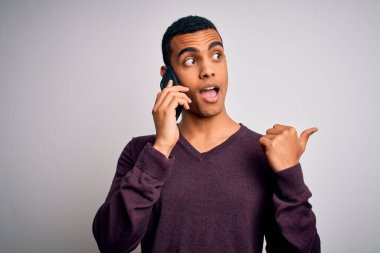 Genç ve yakışıklı Afro-Amerikalı adam akıllı telefondan konuşuyor ve gülümseyen bir gülümsemeyle baş parmağını kaldırıyor.