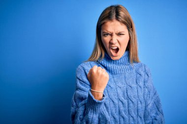 Kışlık yün süveter giyen genç, sarışın bir kadın öfkeli ve öfkeli bir şekilde öfkeyle bağırıyor. Öfke ve agresif kavram.