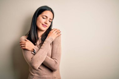 Mavi gözlü genç esmer kadın izole edilmiş beyaz arka plan üzerine günlük süveter giyiyor mutlu ve pozitif, kendinden emin gülümsüyor. Sevgi ve özgüven.