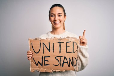 Mavi gözlü, genç, sarışın bir kadın elinde bayrak tutarak mutlu bir yüzle bir fikir ya da soru işaretine şaşırıyor.