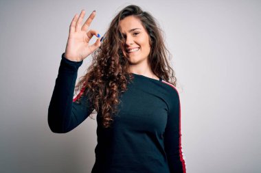 Kıvırcık saçlı genç bir kadın izole edilmiş beyaz arka plan üzerine günlük süveter giyip gülümsüyor ve el ve parmaklarıyla 