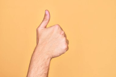 İzole edilmiş sarı arka plan üzerinde parmaklarını gösteren beyaz bir gencin eli başarılı bir onay jesti yapıyor. Başparmak işareti, onaylama ve olumlu sembol ile.