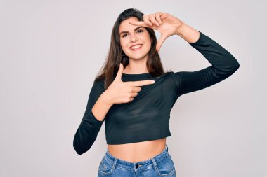 Genç, güzel esmer kadın, sıradan bir süveter ve kot pantolon giyiyor izole edilmiş arka planda gülümsüyor ve elleri ve parmakları mutlu yüzlü bir çerçeve yapıyor. Yaratıcılık ve fotoğrafçılık kavramı.