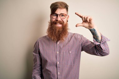 Yakışıklı, kızıl saçlı, sakallı, arka planda gözlük takan, gülümseyen ve el hareketleriyle el hareketi yapan, parmaklarıyla işaret yapan ve kameraya bakan yakışıklı bir iş adamı. Ölçü kavramı.