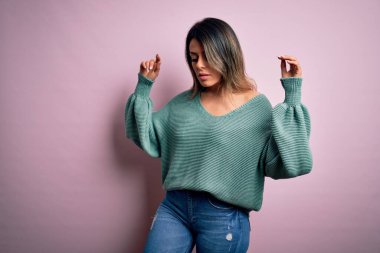 Moda kıyafetleri giyen genç ve güzel bir kadın. Manken, sokak tarzı giyiniyor. Pembe arka planda dikiliyor.