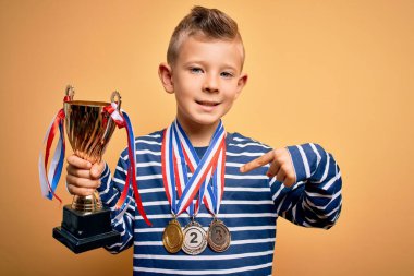 Küçük beyaz çocuk, altın madalyalar ve zafer ödülü takıyor. Arka planda sürpriz bir yüz, kendini işaret ediyor.