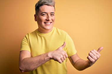 Sarıya boyanmış sarı tişörtlü, genç ve modern bir adam. Arka tarafı işaret ediyor. El ve baş parmakları havada, kendine güvenen.