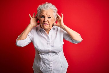 Üst düzey, zarif bir gömlek giymiş, kırmızı arka planda dikilip iki elini de kulak hareketi yaparken duymaya çalışan, dedikoduya meraklı güzel bir kadın. İşitme problemi, sağır